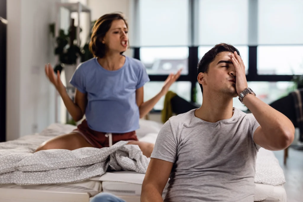 Sex Counseling services in Gurgaon 19 young man feeling stressed out having headache while his girlfriend is arguing with him bedroom