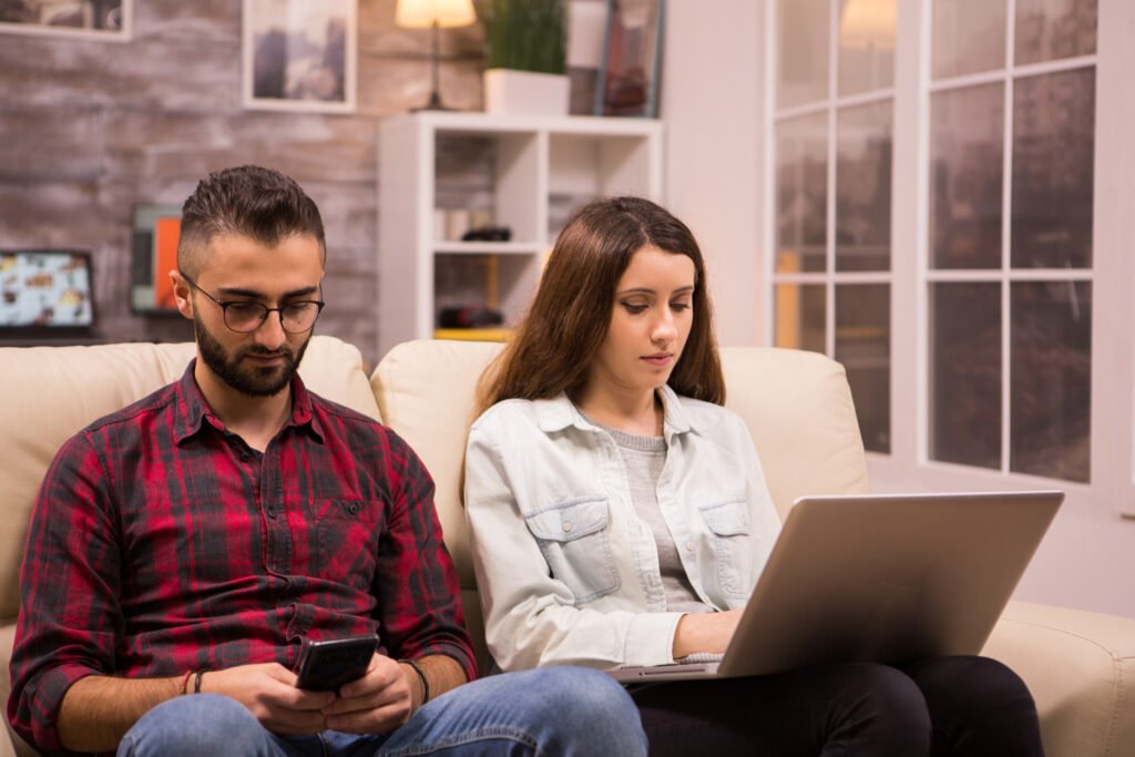 young couple sitting sofa doing online shopping using their laptop phone girlfriend browsing laptop
