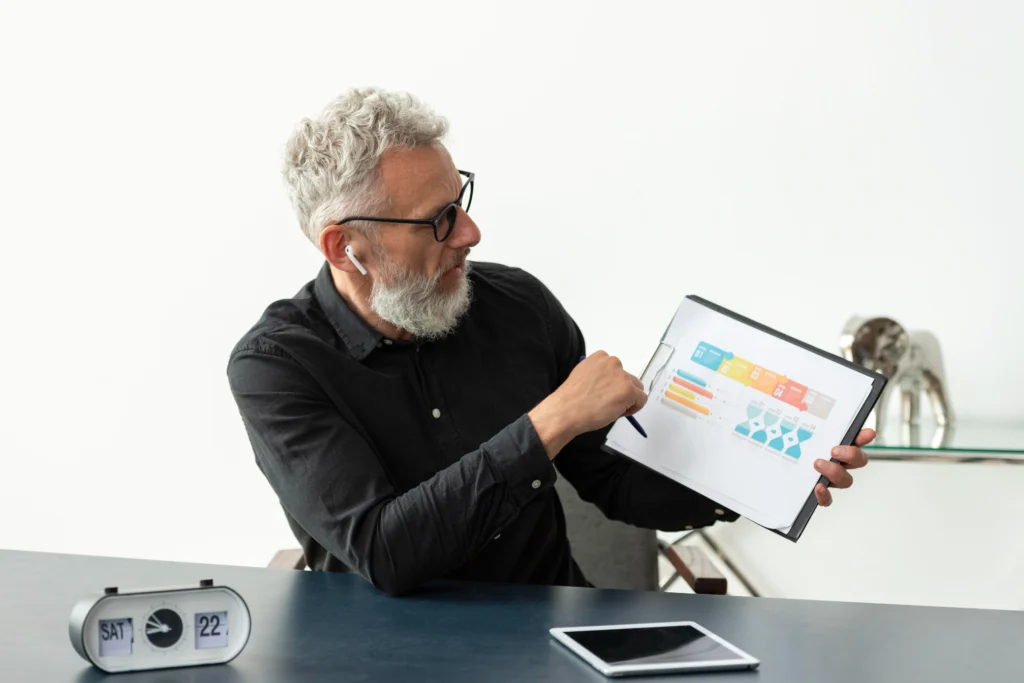 older man home showing graph notepad with tablet desk