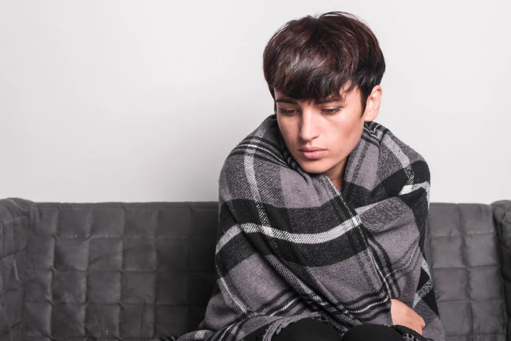sick young woman wrapped blanket sitting sofa