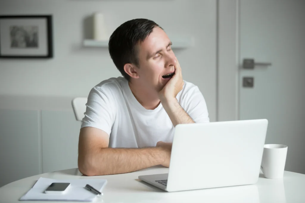 young boring yawn man sitting white desk near laptop