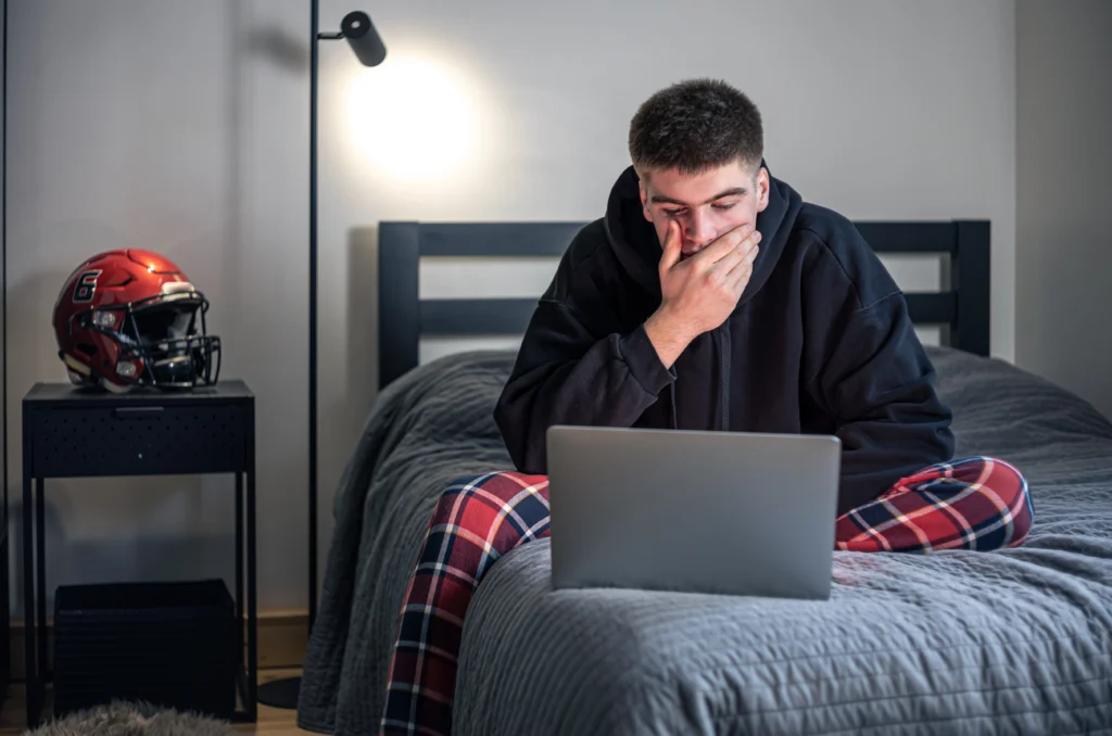 teenager guy sits room bed uses laptop