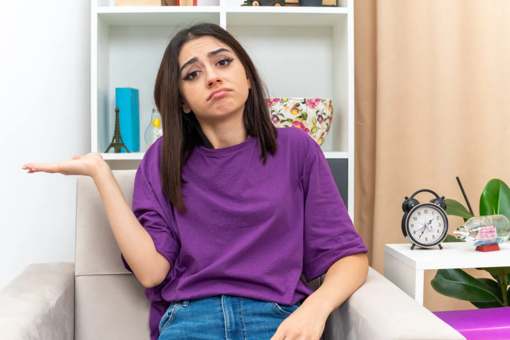 young girl casual clothes looking with sad expression face presenting something with arm her hand sitting chair light living room